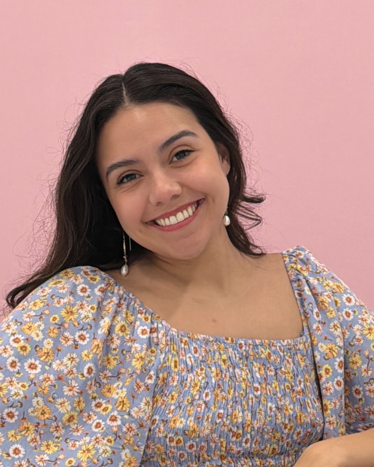 Adriana smiling in a blue floral blouse against a rose-pink backdrop